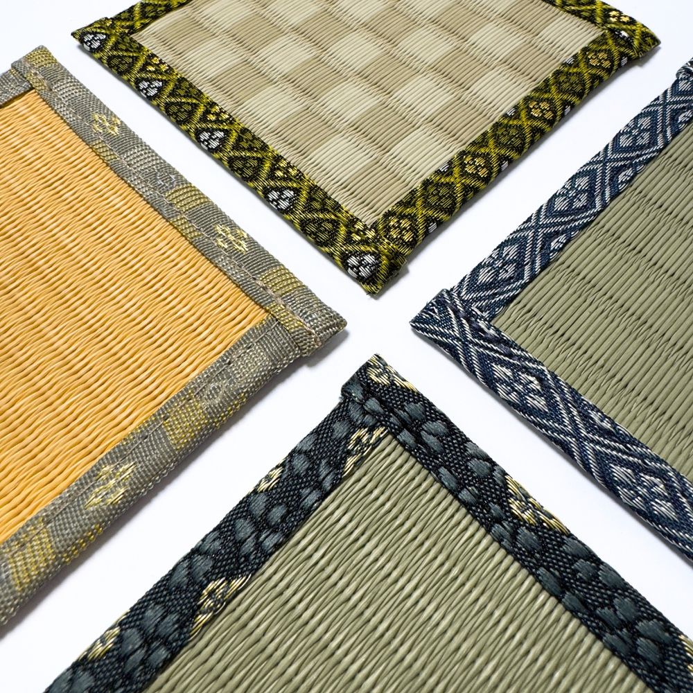 Close up angled view of four tatami coasters in different colours, showing the woven igusa texture and patterned fabric borders.
