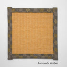 Square tatami coaster with a warm amber coloured igusa centre and a muted grey and olive patterned fabric border.