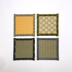 Top down view of four square tatami coasters arranged in a grid, each with a different woven centre and decorative fabric border.